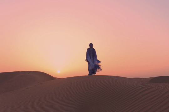 Frau im Gewand auf einer Sandd&uuml;ne im Sonnenuntergang